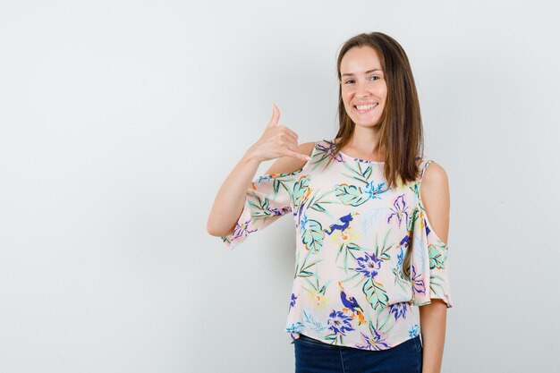 Ragazza che mostra il gesto del telefono in camicia, jeans e che sembra gioiosa. vista frontale.