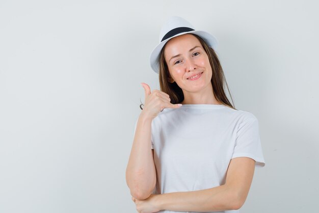 Ragazza che mostra il gesto del telefono in maglietta bianca, cappello e in cerca utile. vista frontale.