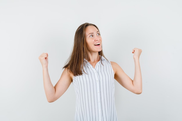 Ragazza che mostra il gesto del vincitore in maglietta e che sembra beata, vista frontale.