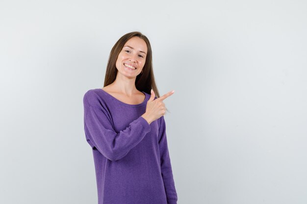 Ragazza che mostra il gesto della pistola in camicia viola e che sembra felice, vista frontale.