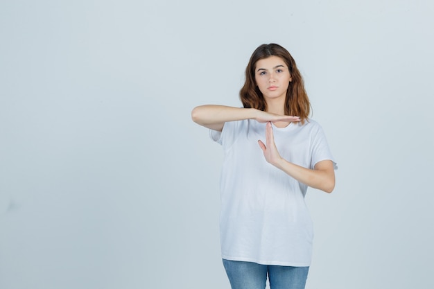 Ragazza che mostra il gesto di pausa di tempo in maglietta bianca e guardando fiducioso, vista frontale.