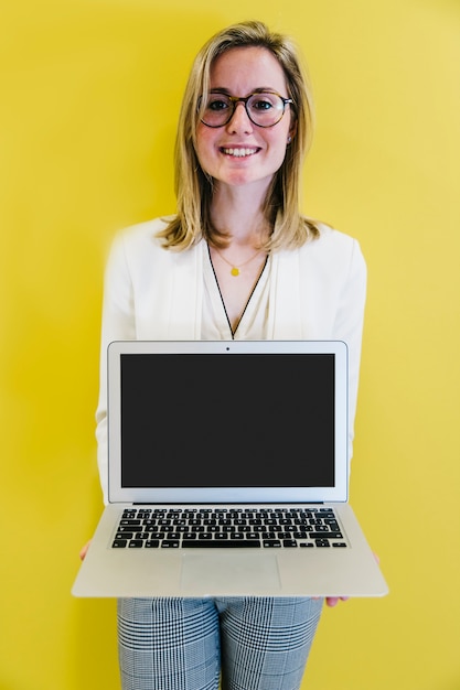 Ragazza che mostra nuovo computer portatile su giallo