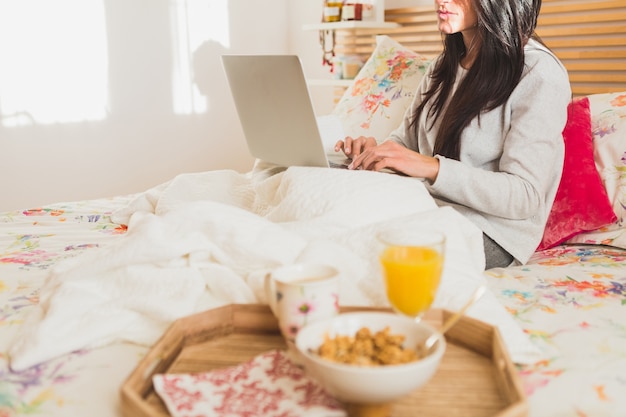 Ragazza che per mezzo del suo computer portatile prima di fare colazione