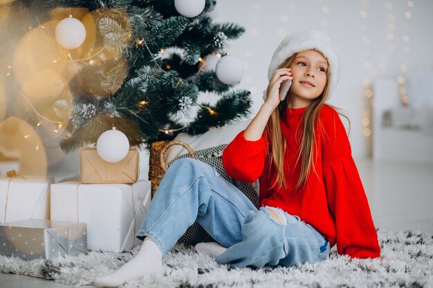 Ragazza che per mezzo del telefono dall'albero di Natale a Natale