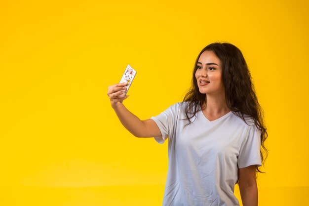 Ragazza che prende il suo selfie sul telefono cellulare sulla parete gialla.