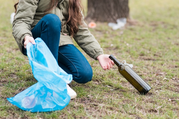 Ragazza che pulisce una bottiglia di vetro da terra