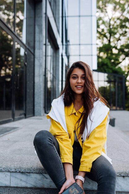 Ragazza che riposa sui gradini. Attraente ragazza alla moda allegro alla moda hipster che cammina per le strade della città.