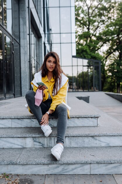 Ragazza che riposa sui gradini. Attraente ragazza alla moda allegro alla moda hipster che cammina per le strade della città.