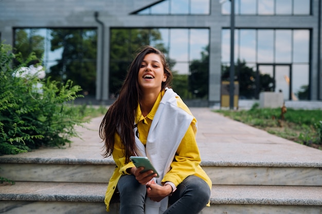 Ragazza che riposa sui gradini. Attraente ragazza alla moda allegro alla moda hipster che cammina per le strade della città.