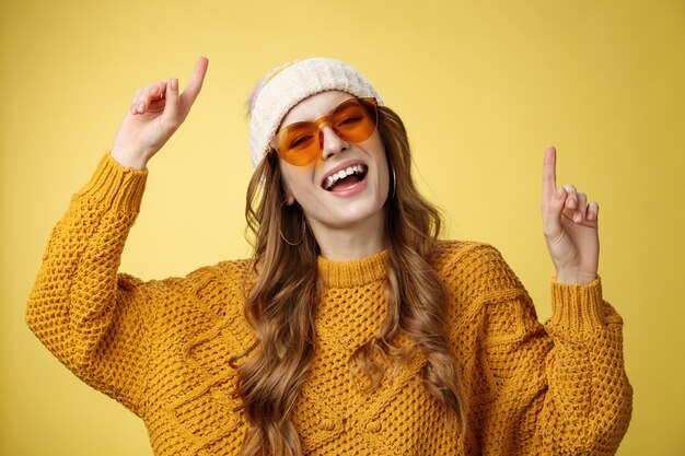 Ragazza che si gode la festa si diverte sorridendo ampiamente felice guardando la telecamera alzando le dita indice fino a ballare ca...