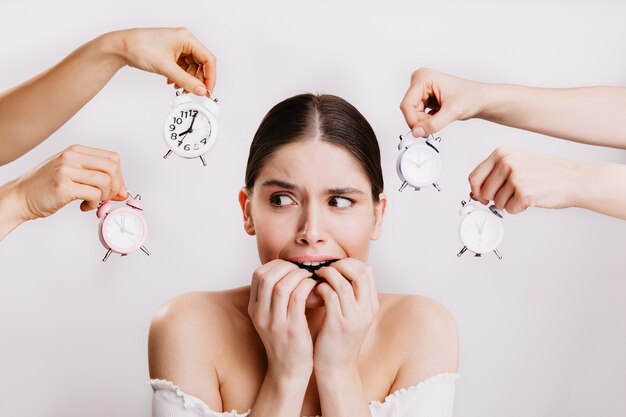 Ragazza che si morde le dita per la paura. La donna nella paura pone contro il muro delle mani che tengono l'orologio.