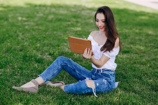 Ragazza che si siede in un parco con una tavoletta in mano