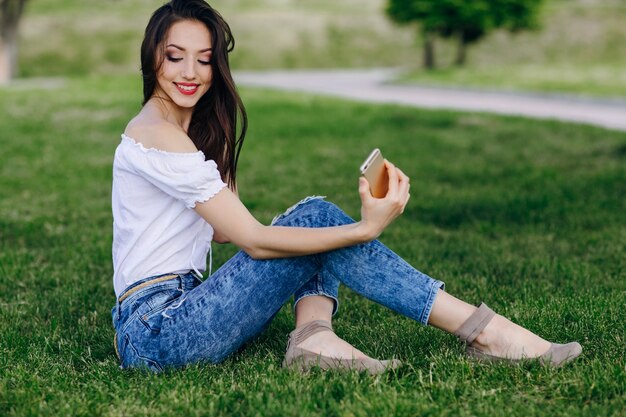 Ragazza che si siede in un parco fare una foto di auto, mentre sorridente e toccare i capelli