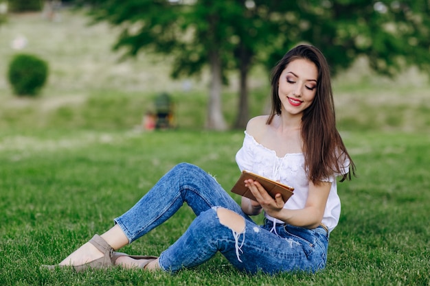 Ragazza che si siede in un parco guardando con un sorriso una tavoletta