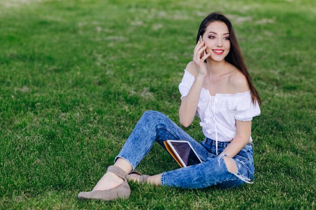 Ragazza che si siede in un parco, parlando al telefono, mentre sorridendo