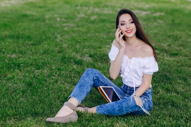 Ragazza che si siede in un parco, parlando al telefono