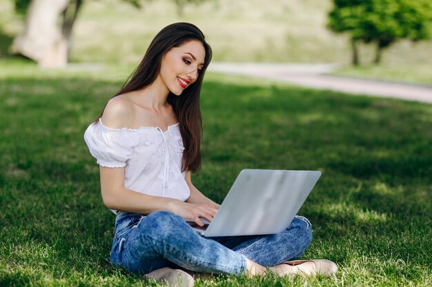 Ragazza che si siede in una digitazione parco sul suo computer portatile