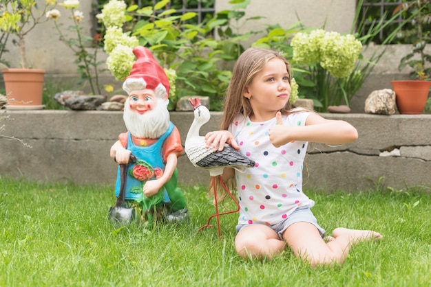 Ragazza che si siede nel giardino che mostra pollice sul segno