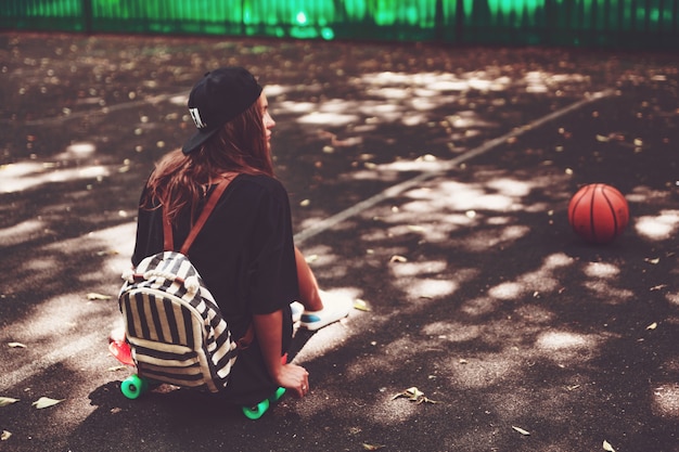 Ragazza che si siede sulla shortboard arancione di plastica del penny sull'asfalto in protezione