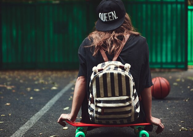 Ragazza che si siede sulla shortboard arancione di plastica del penny sull'asfalto in protezione