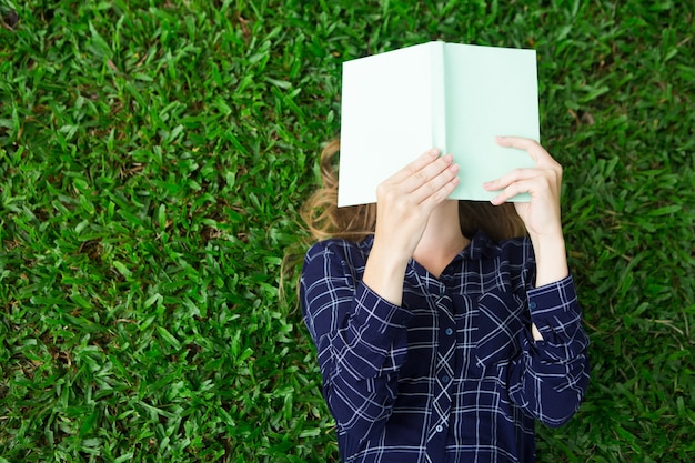 Ragazza che si trova sull&#39;erba e libro di lettura