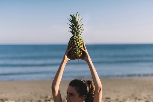 Ragazza che solleva ananas in spiaggia