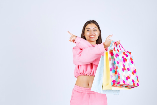 Ragazza che tiene i sacchetti della spesa variopinti e che indica da qualche parte in su.