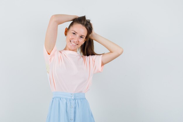 Ragazza che tiene i suoi capelli in maglietta, gonna e che sembra allegra. vista frontale.