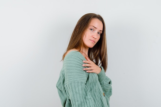 Ragazza che tiene la mano sul petto in maglieria e dall'aspetto affascinante, vista frontale.