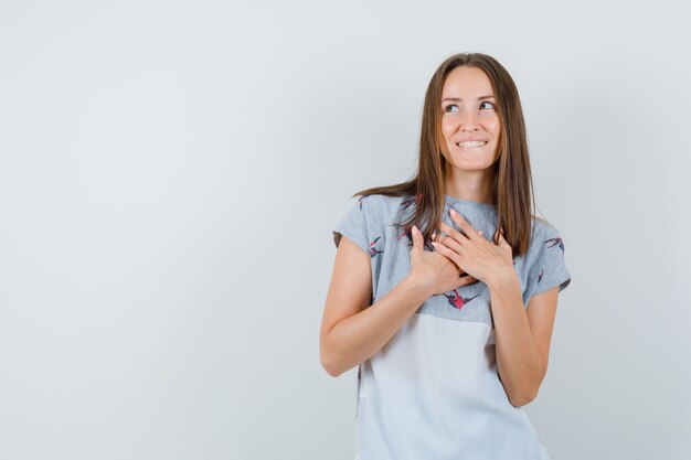 Ragazza che tiene le mani sul petto in t-shirt e dall'aspetto sognante, vista frontale.