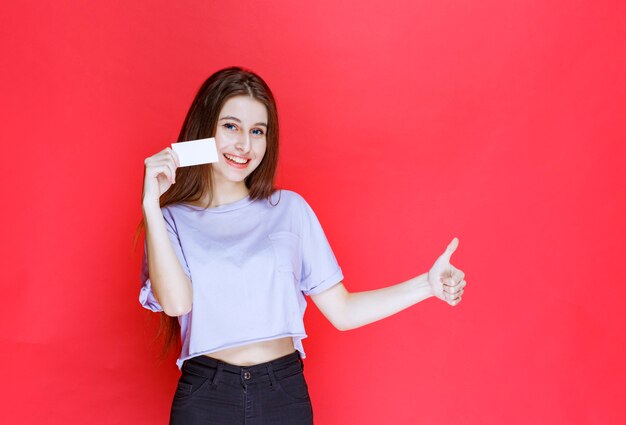 Ragazza che tiene un biglietto da visita e che mostra il segno positivo della mano.