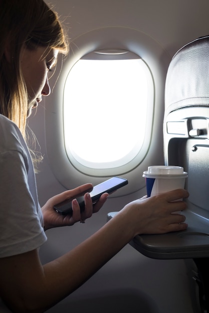 Ragazza che tiene un caffè e che esamina telefono