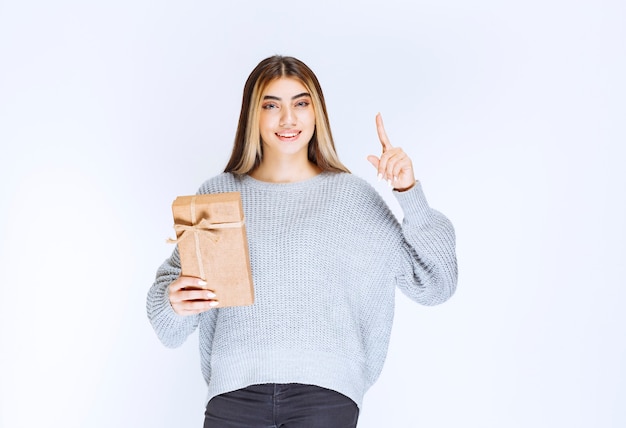 Ragazza che tiene una scatola regalo di cartone e indica un ricevitore da parte.