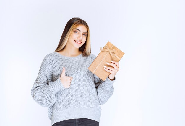 Ragazza che tiene una scatola regalo di cartone e mostra pollice in su.