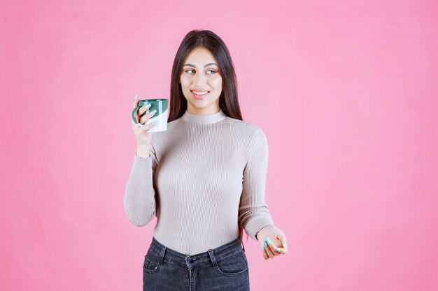 Ragazza che tiene una tazza da caffè di colore verde bianco e si sente positivo