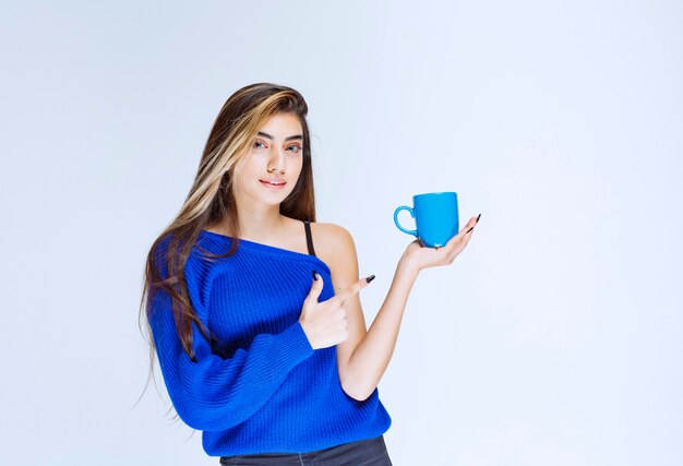 Ragazza che tiene una tazza di caffè blu e che mostra a qualcuno.