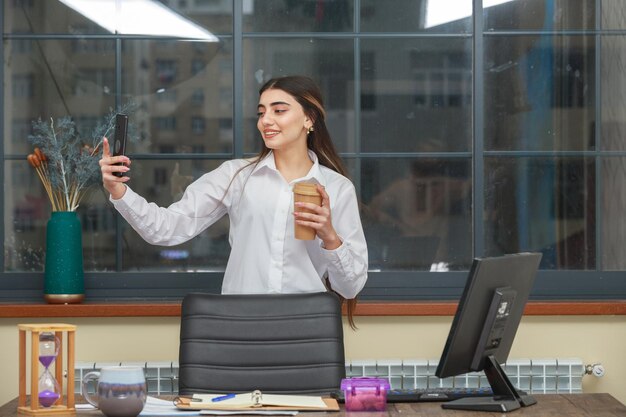 Ragazza che tiene una tazza di caffè e si fa selfie