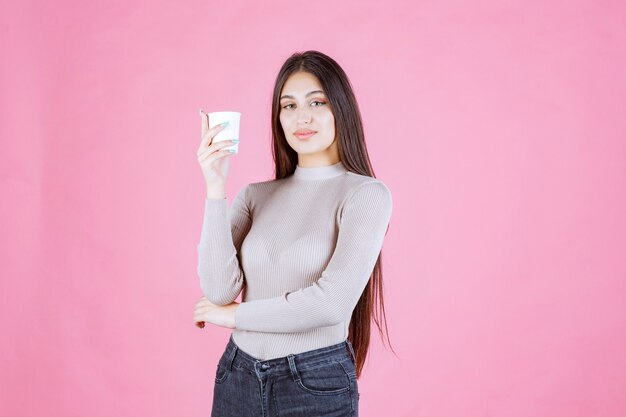 Ragazza che tiene una tazza di caffè usa e getta bianca, promuovendola o annusando il caffè fresco