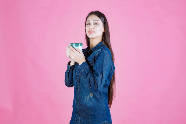 Ragazza che tiene una tazza di caffè verde bianca e un odore