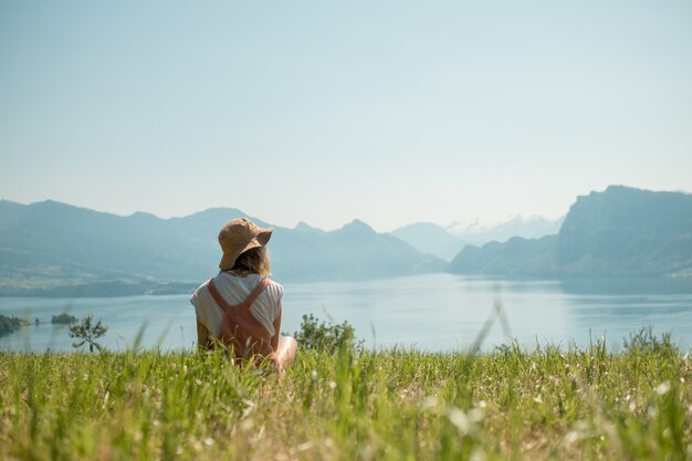 Ragazza con aveva seduto sul prato verde vicino al lago