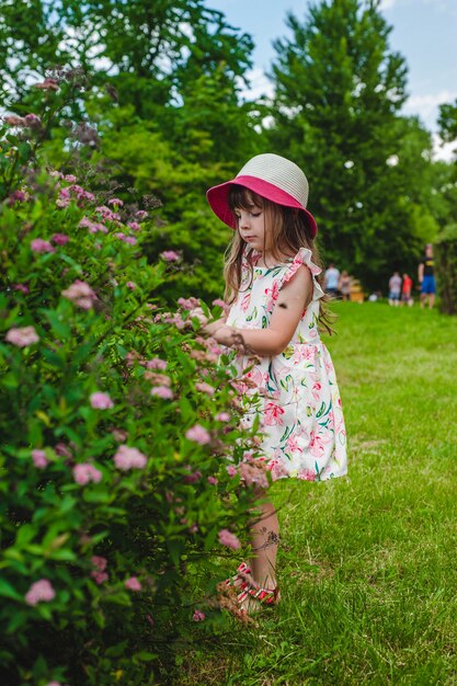 Ragazza con cappello guardando i fiori di un cespuglio