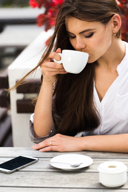 Ragazza con i capelli lunghi beve caffè seduto nel ristorante