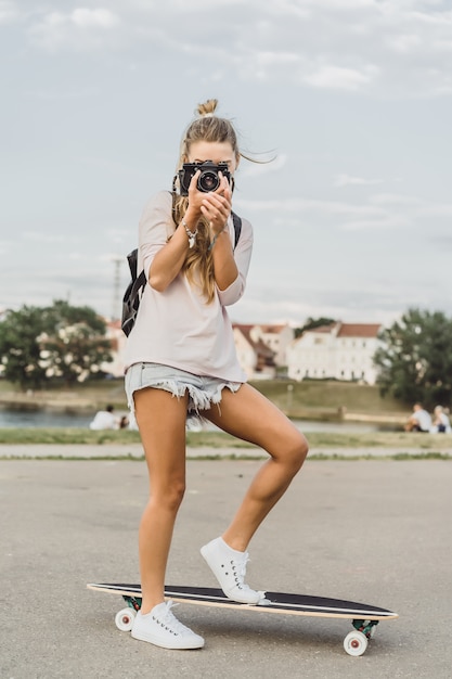 ragazza con i capelli lunghi con skateboard fotografando sulla fotocamera. strada, sport attivi