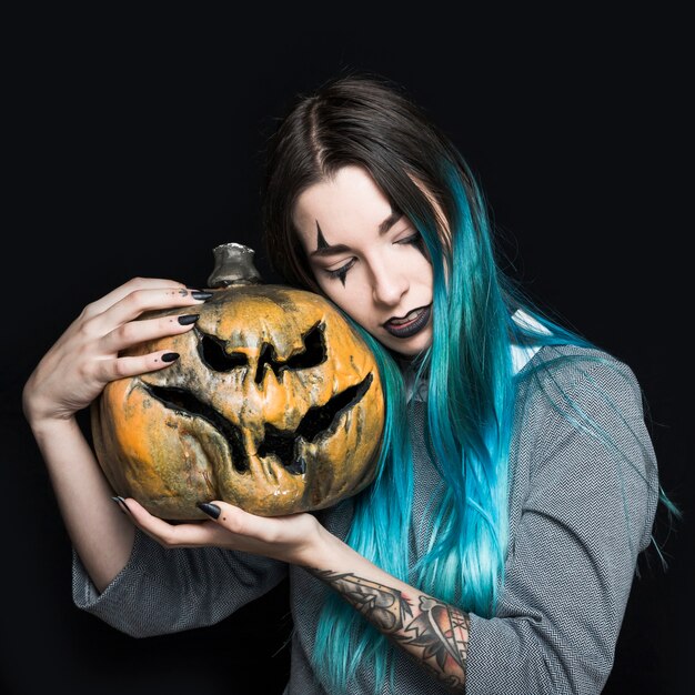 Ragazza con il trucco del pagliaccio che tiene zucca terrificante