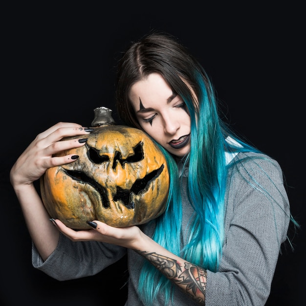 Ragazza con il trucco del pagliaccio che tiene zucca terrificante