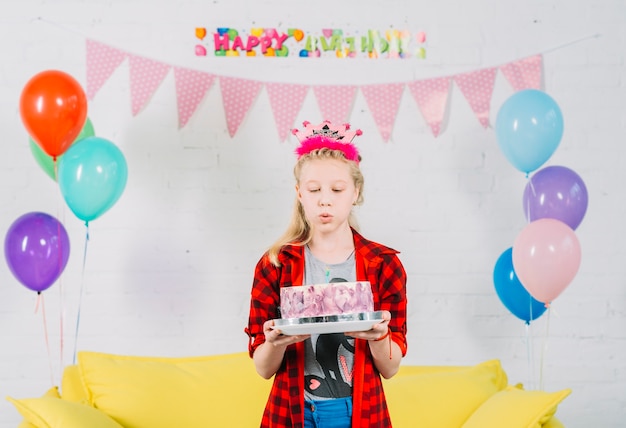 Ragazza con la torta di compleanno soffiando la candela