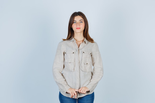 Ragazza con le mani davanti a lei in camicia beige, jeans e dall'aspetto affascinante. vista frontale.