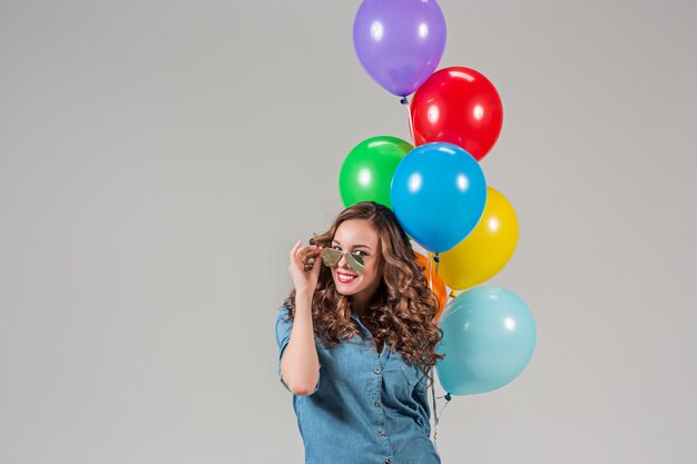 Ragazza con occhiali da sole e mazzo di palloncini colorati