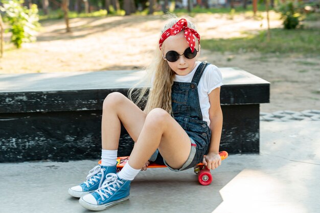 Ragazza con occhiali da sole seduto su skateboard