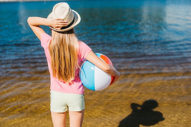 Ragazza con palla gonfiata guardando acqua